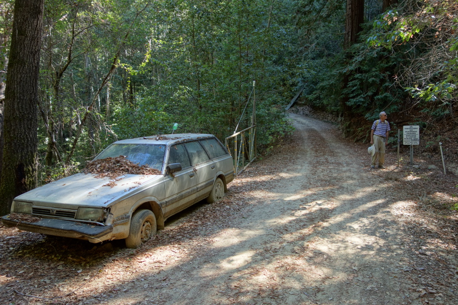 An abandoned car stuck in dried mud guards the gate.