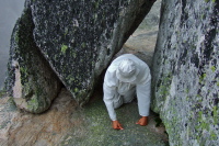 David crawls through rocks to get to the hidden ledge.