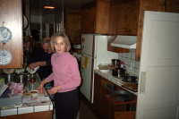 Julie does dishes while David scoops leftovers into a jar.