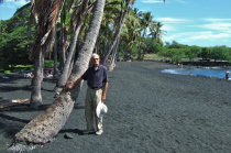 David stands before a line of coconut palms at Punalu'u black sand beach.